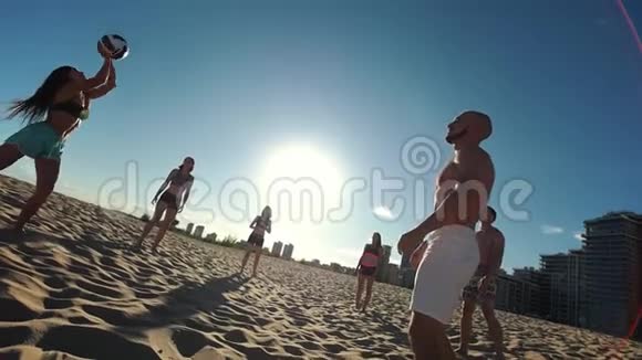 美丽的年轻人在夏天的傍晚在阳光下打沙滩排球视频的预览图