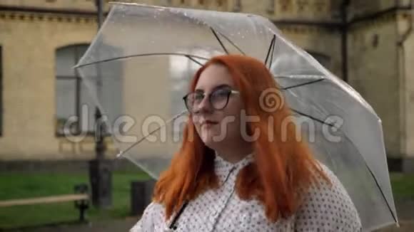 戴眼镜的肥姜女孩在雨天的公园里散步撑着伞侧视视频的预览图
