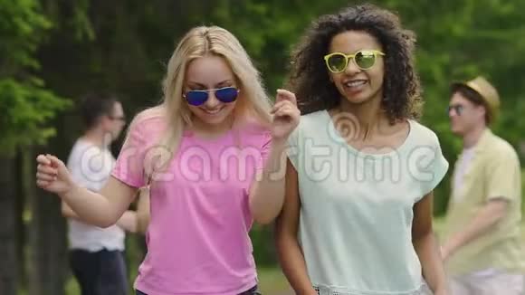 两个年轻的快乐女人在聚会上随着音乐跳舞男人在公园里享受夏天视频的预览图