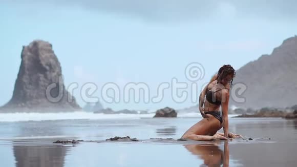 美丽的女人穿着泳装在海滩上跳舞沙滩上有黑色的沙子靠近大海视频的预览图