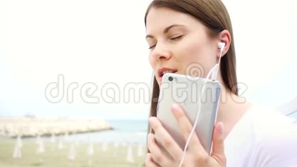 年轻女子独自在海滩上使用手机女性通过手机听音乐慢动作唱歌视频的预览图