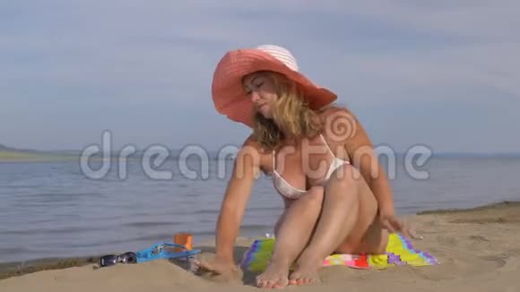 美丽的女人坐在海滩上从她的手里倒沙子视频的预览图