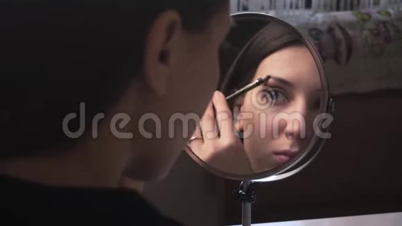 美丽的女孩照镜子用铅笔画眉毛化妆视频的预览图