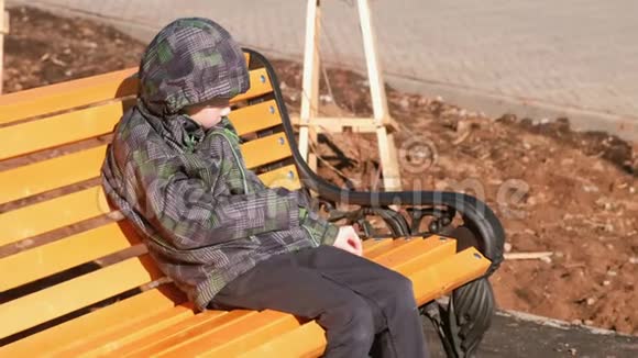 男孩坐在公园的长凳上用石头划伤长凳视频的预览图