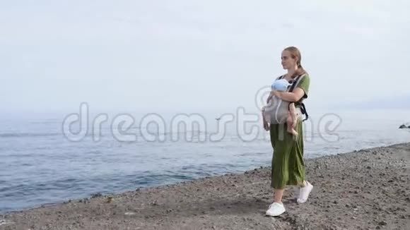 夏天宝宝和妈妈在海上幸福的家庭在户外散步儿童在一个载体背包妇女与妇女视频的预览图