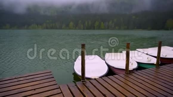 小船漂浮在靠近木墩的湖面上平静的山湖表面雾蒙蒙的山林视频的预览图