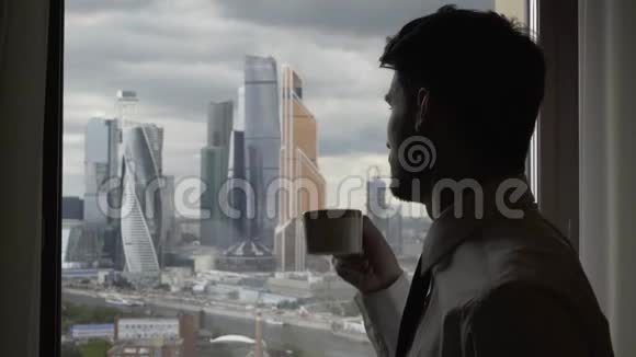 男人喝着咖啡从窗户望着莫斯科的城楼阴天视频的预览图