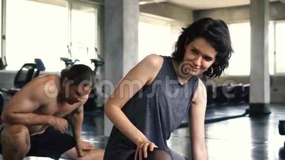 年轻的女人和男人在健身房地板上伸展腿两个人在室内工作视频的预览图