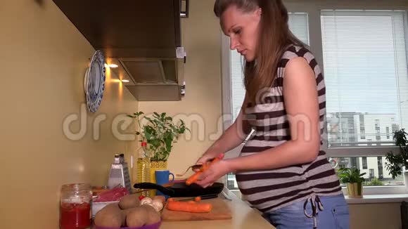 漂亮的孕妇在厨房里剥胡萝卜蔬菜视频的预览图