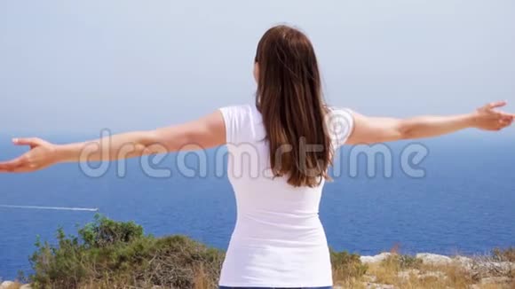 微笑的女人在悬崖上与蓝色的大海搏斗无忧无虑的女电车慢动作视频的预览图