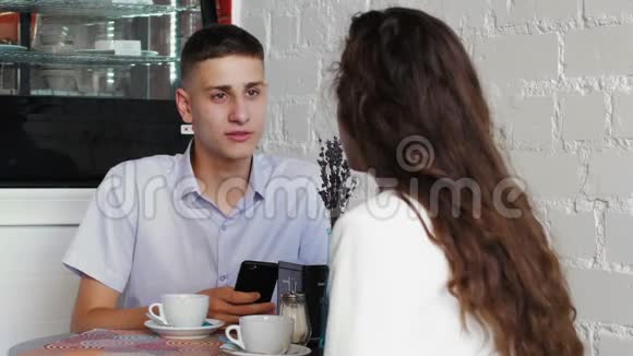 穿蓝色衬衫的人在咖啡馆里用电话付账一对年轻夫妇在咖啡馆的约会视频的预览图