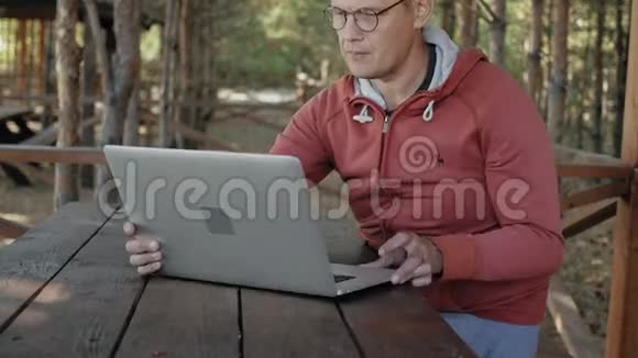 一个成熟的男人正在大自然中的户外工作在他的假期里年老的森林人用他的笔记本电脑发电子邮件视频的预览图