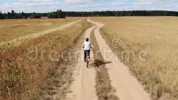 一个年轻的女人骑着自行车在马路上穿过田野从上面看空中摄影视频的预览图