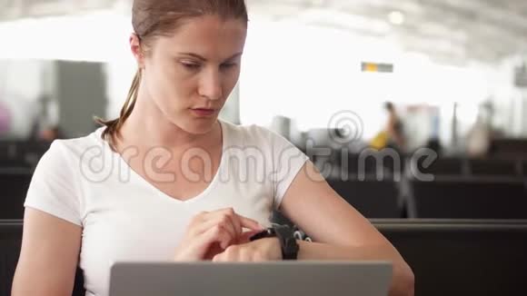 女人坐在机场候机室里拿着笔记本电脑休闲女商人在智能手表上发送信息视频的预览图