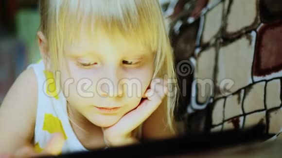 一个6岁女孩躺在沙发上玩平板电脑的肖像视频的预览图