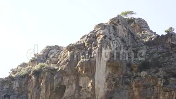 一座山的岩石坡和一棵树在明亮的蓝天背景下生长在山顶上艺术岩石的底部景色视频的预览图