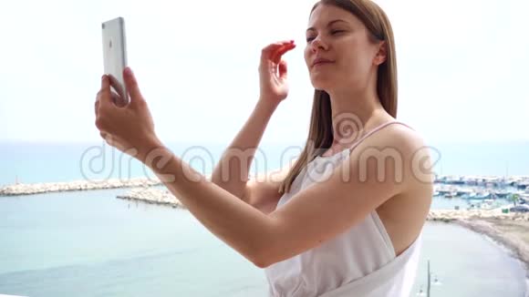 女人在阳台上使用手机女性在手机上慢动作欣赏海景并拍照视频的预览图