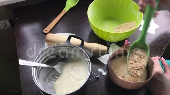 女人在蛋糕模具上加入海绵蛋糕做一个饼干面包屑和牛奶果冻蛋糕在桌子的表面是视频的预览图