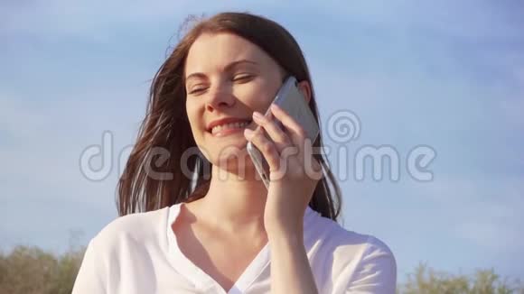 女人用手机对抗蓝天微笑女性通过手机慢动作与朋友交谈视频的预览图