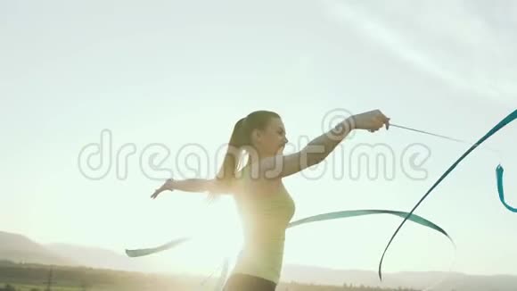 韵律体操运动体衣中的女孩在日落或室外用蓝色丝带表演体操视频的预览图
