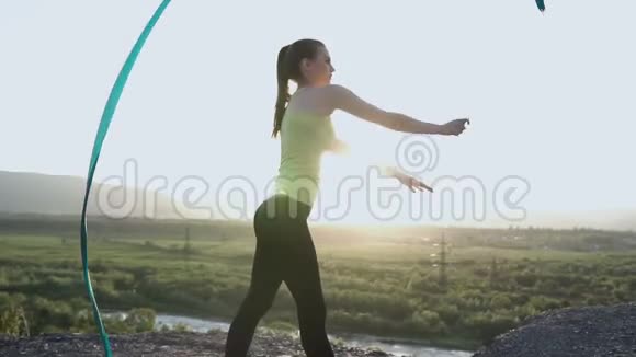迷人的女体操运动员在日落背景下用丝带在山顶跳舞有节奏的体操运动员体育女孩视频的预览图