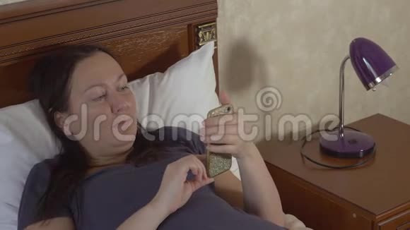 女人浏览她的智能手机躺在床上视频的预览图