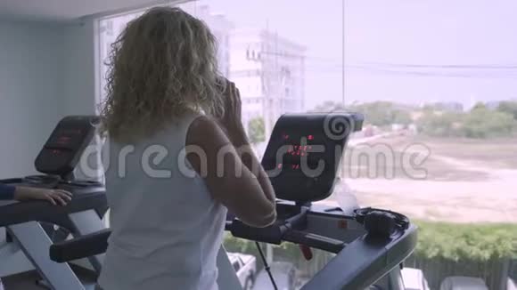 老年妇女在健身房的跑步机上订婚女人在电话里说话做跑步机视频的预览图