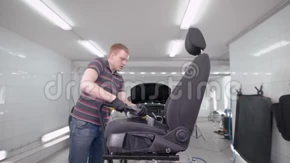 红发男子正在清洁洗车期间在一间自动服务的房间里徘徊着黑色的汽车座椅视频的预览图