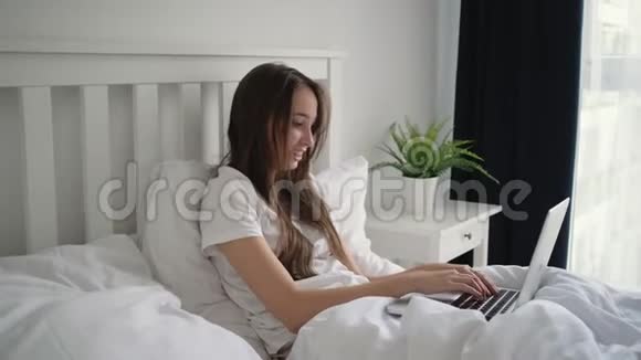 早上坐在床上的女人正在用笔记本电脑打字视频的预览图