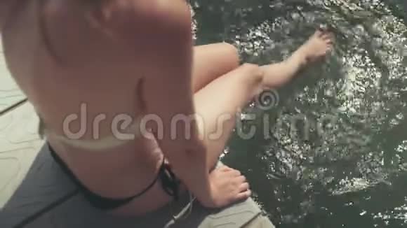 美丽的比基尼女郎坐在湖边的木墩上享受时光视频的预览图