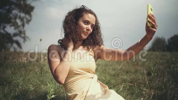 年轻漂亮的女人坐在草地上打电话自拍视频的预览图