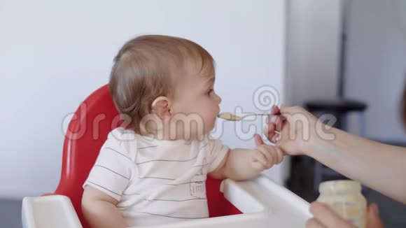 一个可爱的孩子用勺子喂婴儿食物的肖像母亲用美味的食物喂儿子视频的预览图