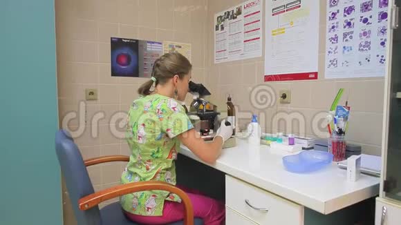 一个穿着绿色连衣裙和白手套的年轻女子透过桌子上的显微镜看着视频的预览图