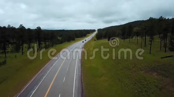 夏季多云间阴天绿林丘陵之间的公路公路上无人机低飞车水马龙视频的预览图