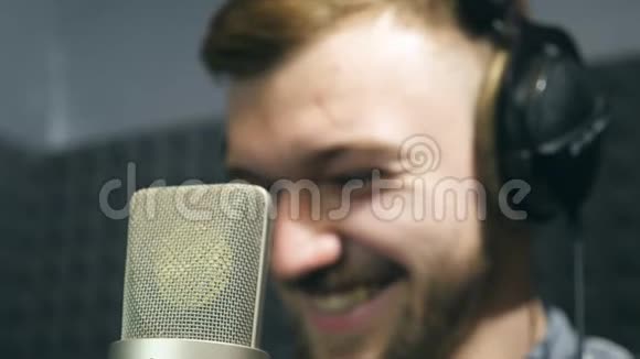 在工作过程中男歌手在耳机中微笑的声音工作室的肖像年轻人的感情记录视频的预览图