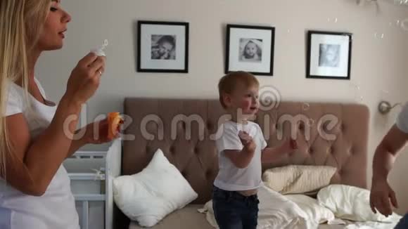 可爱的妈妈玩儿子看肥皂泡男孩高兴地跳在床上视频的预览图