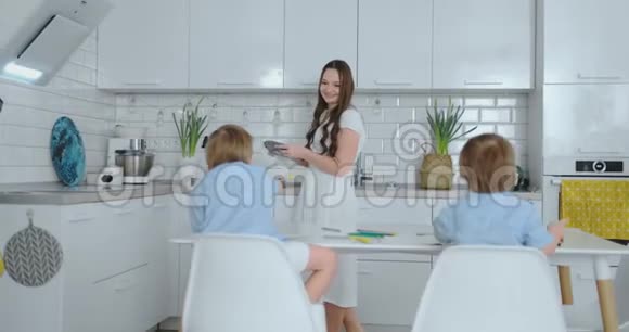 妈妈在厨房洗碗两个儿子坐在办公桌前用彩色铅笔在纸上画画视频的预览图