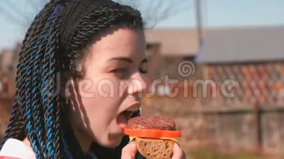 有蓝色辫子的年轻女人在户外吃三明治面包小切片胡椒和奶酪视频的预览图