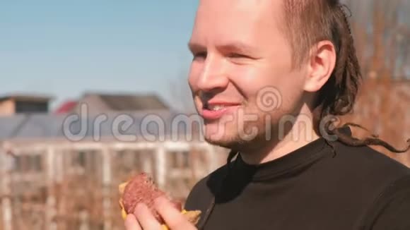 头发长得可怕的年轻人在户外吃三明治和面包切丁胡椒和奶酪视频的预览图
