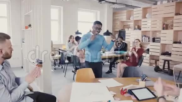 快乐的黑人做滑稽的胜利舞蹈庆祝成就多种族同事在现代办公室4K鼓掌视频的预览图