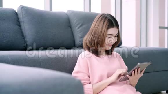 亚洲女人在客厅里躺在家里的沙发上用平板电脑快乐女性使用平板电脑与她的朋友进行视频通话视频的预览图
