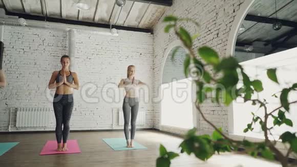 年轻苗条的女人正在上午的瑜伽课上在灯光工作室明亮的垫子上做太阳敬礼的复杂动作健康视频的预览图