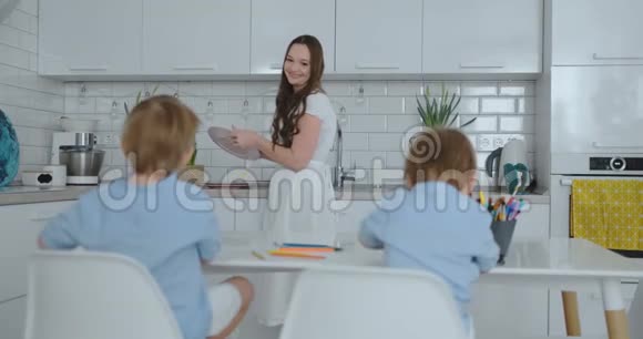 妈妈在厨房洗碗两个儿子坐在办公桌前用彩色铅笔在纸上画画视频的预览图