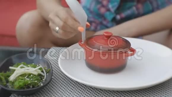 有魅力的年轻白种人女人打开一个泥锅在日本餐馆的露天露台上品尝汤味视频的预览图
