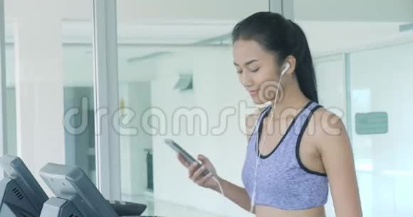 亚洲女孩在跑步机上跑步在健身房用智能手机自拍视频的预览图