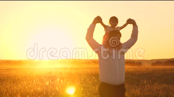 快乐的爸爸带着心爱的孩子在日落时走在田野上慢动作视频的预览图