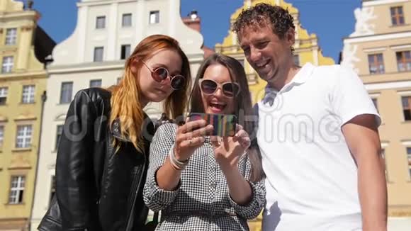 两个女孩和一个男人的户外肖像黑发手拿黑色手机三个朋友在用智能手机视频的预览图