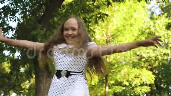 一位留着长发的漂亮女孩在一个夏日公园里穿着一件带豌豆的白裙子双手交叉微笑着视频的预览图