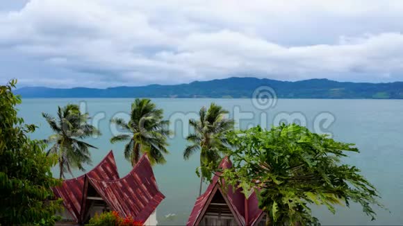 苏门答腊北部萨摩西尔岛传统巴塔克风格屋顶多云天气下托巴湖的电影视频的预览图