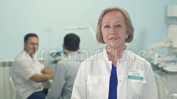 资深女医生看镜头而男医生在后台与病人交谈视频的预览图